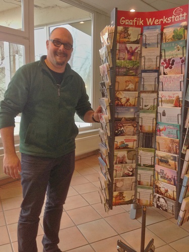 Matthias Hübner am Kiosk-Ständer mit den SiKra-Liedpostkarten in der Mitte